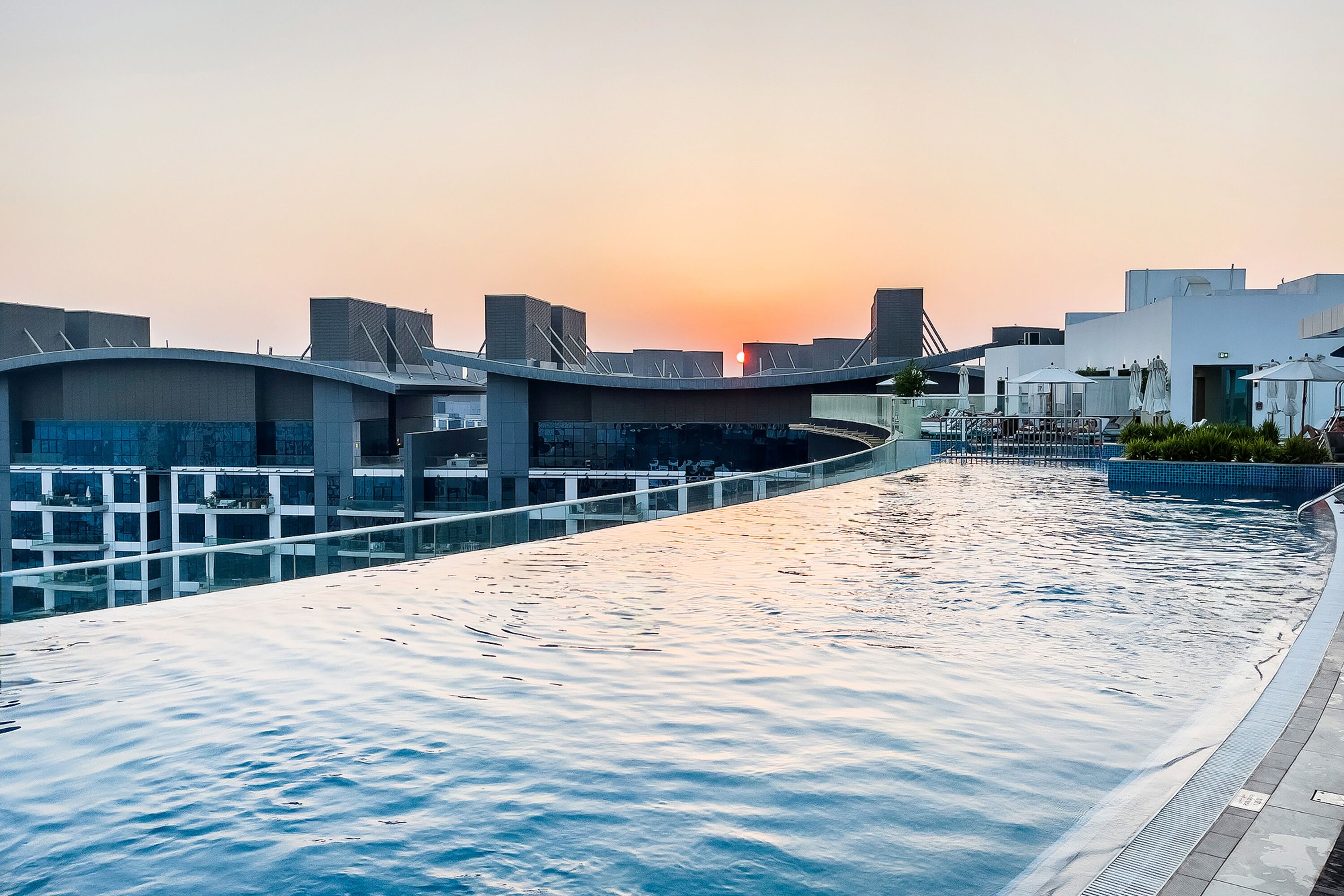 Une piscine sur le toit offrant une vue sur le coucher du soleil, une architecture moderne et une balustrade en verre.