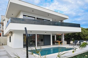Una casa moderna de dos pisos con piscina, ventanas amplias y un balcón.