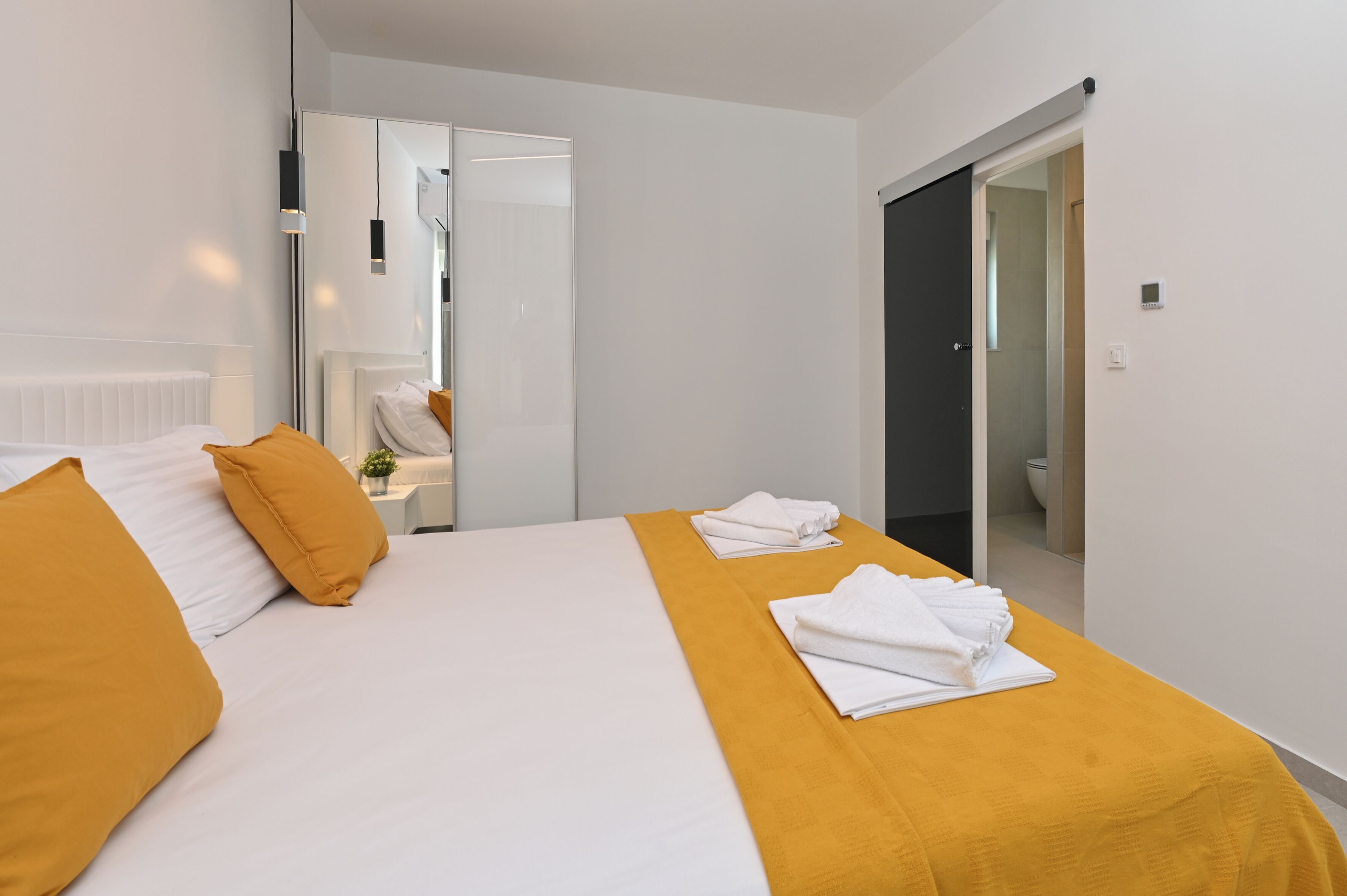 A hotel room with a bed, a bathroom visible through an open door, and a mirror on the wall.