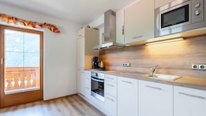 Moderni keittiö, jossa on valkoiset kaapit, ruostumattomasta teräksestä valmistettu mikroaaltouuni ja sisäänrakennettu uuni.