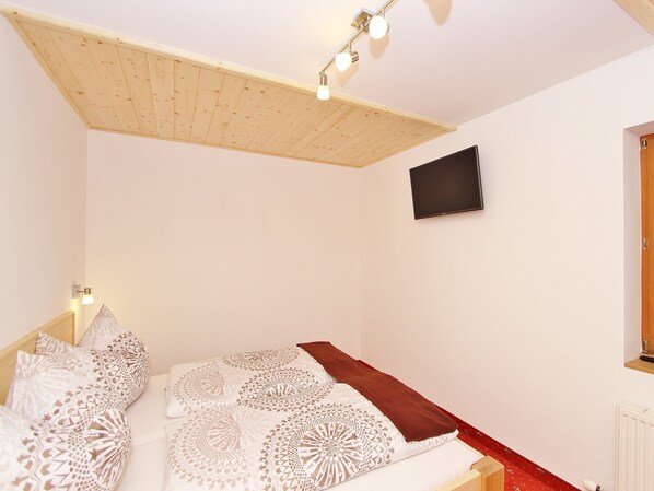 A bedroom with a sloped ceiling, a mounted TV, and patterned bedding.