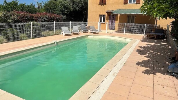Una piscina rectangular con un borde de baldosas, rodeada por una cerca blanca.