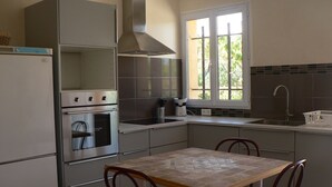 Una cocina compacta con horno integrado, extractor de acero inoxidable, ventana con vistas y zona de comedor con mesa y sillas.