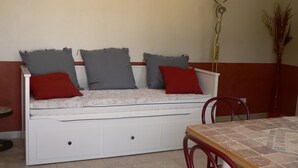 Un sofá blanco con tres almohadas, una mesita y una lámpara en una habitación con suelo de baldosas.