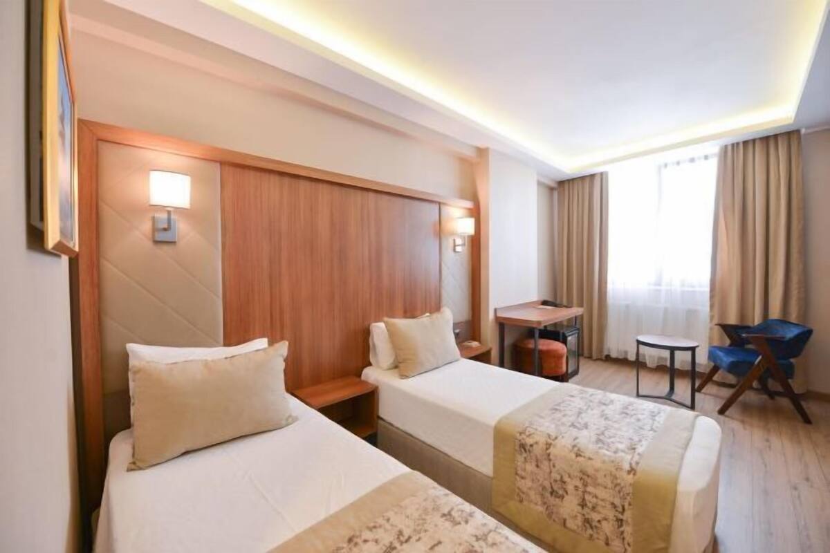 Habitación de hotel con dos camas, un escritorio, una silla y una ventana con cortinas.