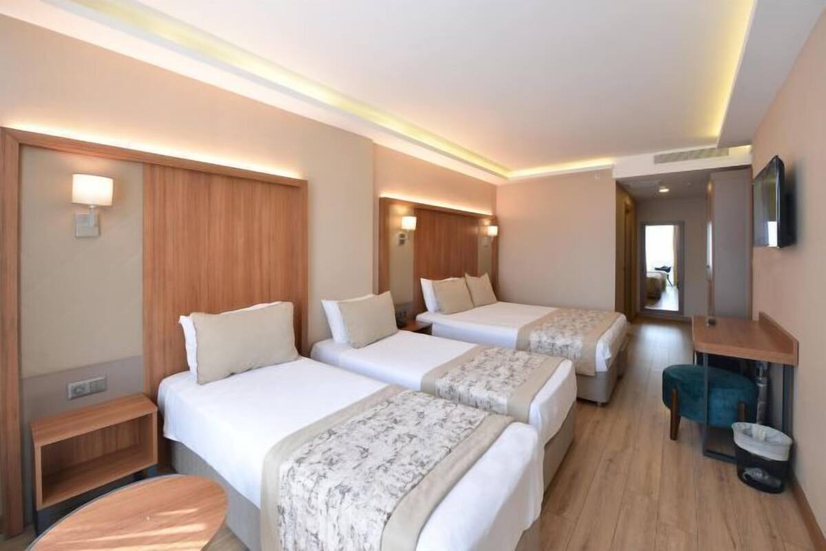 Habitación de hotel con tres camas, cabecero de madera, un escritorio pequeño y un espejo.