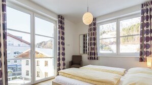 A bedroom with a large bed, two windows, a chair, and a hanging light fixture. - Apartment in Leogang near Ski Slopes (Leogang)