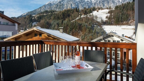 A balcony with a table set for two, overlooking a snowy mountain range. - Apartment in Leogang near Ski Slopes (Leogang)