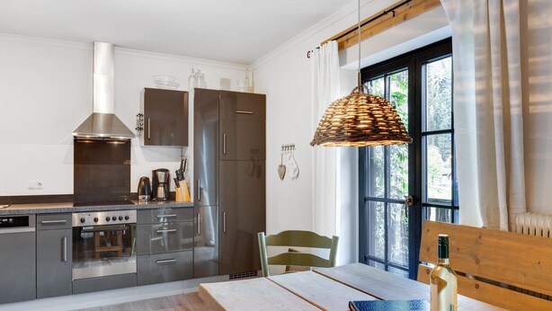 A modern kitchen with stainless steel appliances, a wooden dining table, and a large window with curtains. - Chalet in Leogang near Ski Lifts (Leogang)