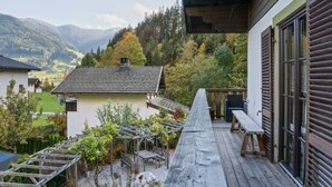 A wooden deck with a bench and a table, surrounded by a garden with grapevines and a view of a mountain landscape. - Chalet in Leogang near Ski Lifts (Leogang)