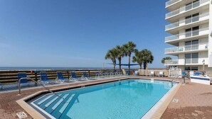 Une piscine avec des chaises bleues, des palmiers et une vue sur l’océan.