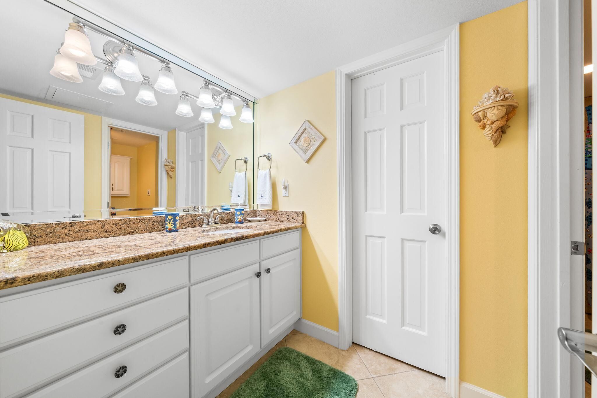 A bathroom with a white vanity, a large mirror, and a yellow accent wall.