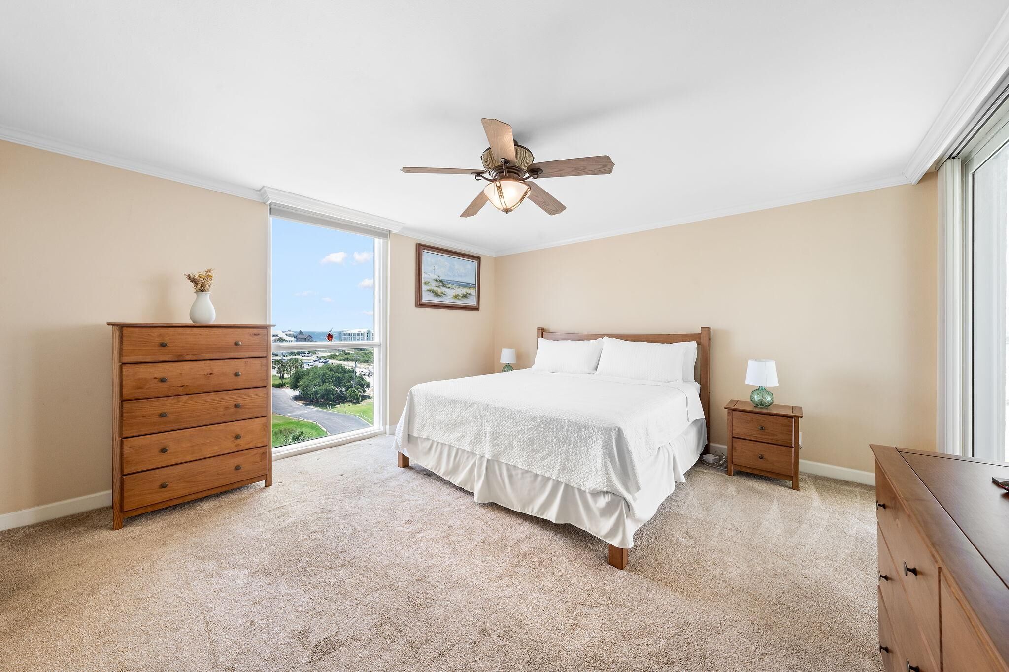 Une chambre à coucher comprenant un lit, une commode en bois, une table de chevet et un ventilateur de plafond.