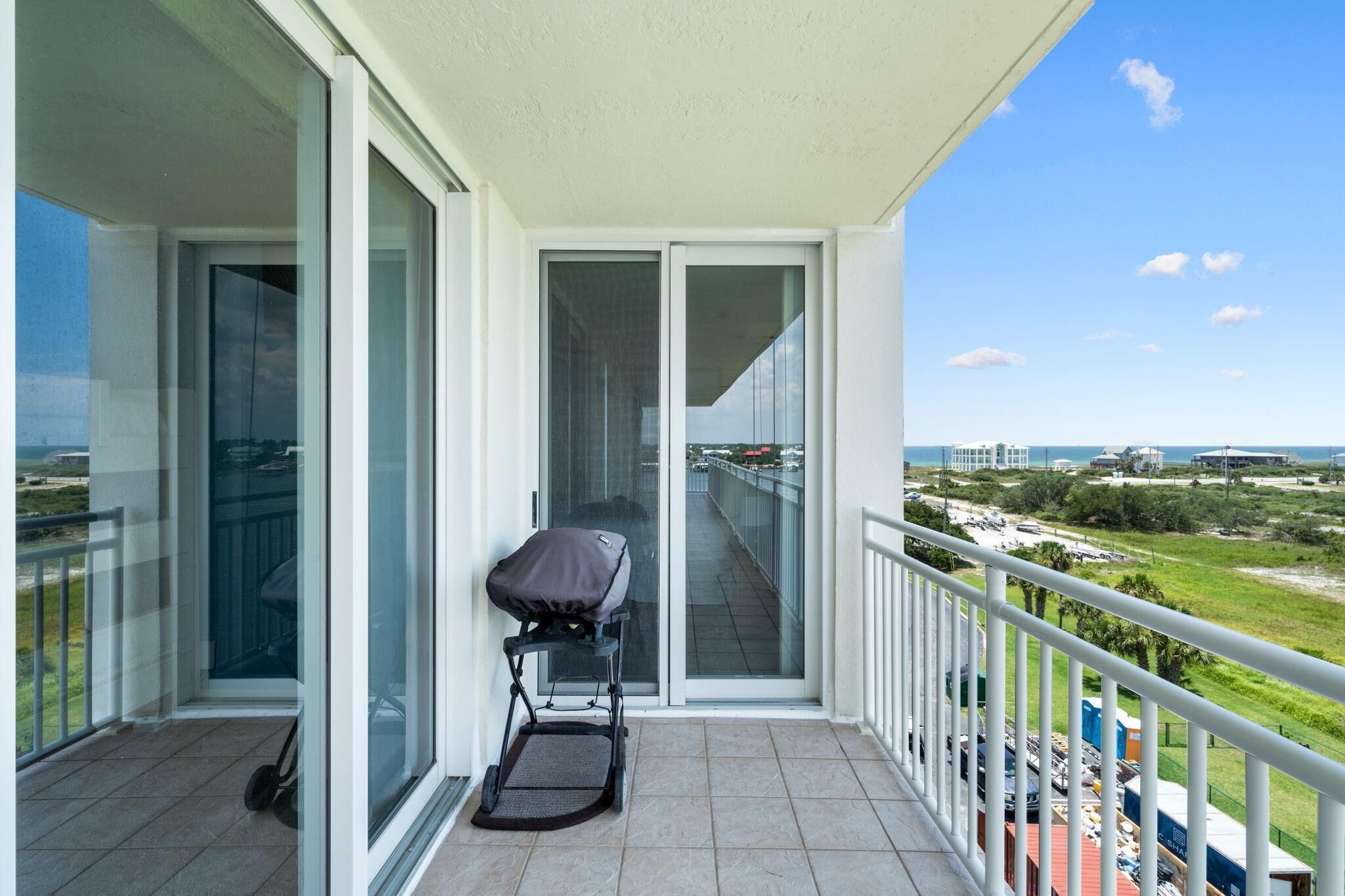 A balcony with a stroller, glass doors leading to a view of the beach and cityscape.
