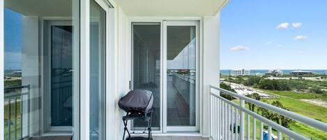 A balcony with a stroller, glass doors leading to a view of the beach and cityscape.