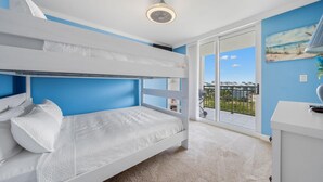 Un lit superposé avec une literie blanche, un bureau blanc et un balcon offrant une vue sur la ville.