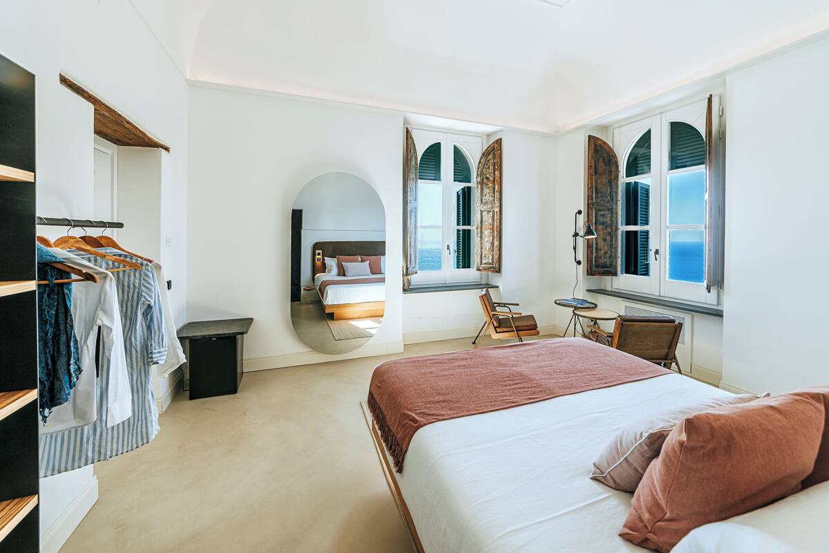 Quarto com cama, uma cadeira, escrivaninha, guarda-roupa e espelho.