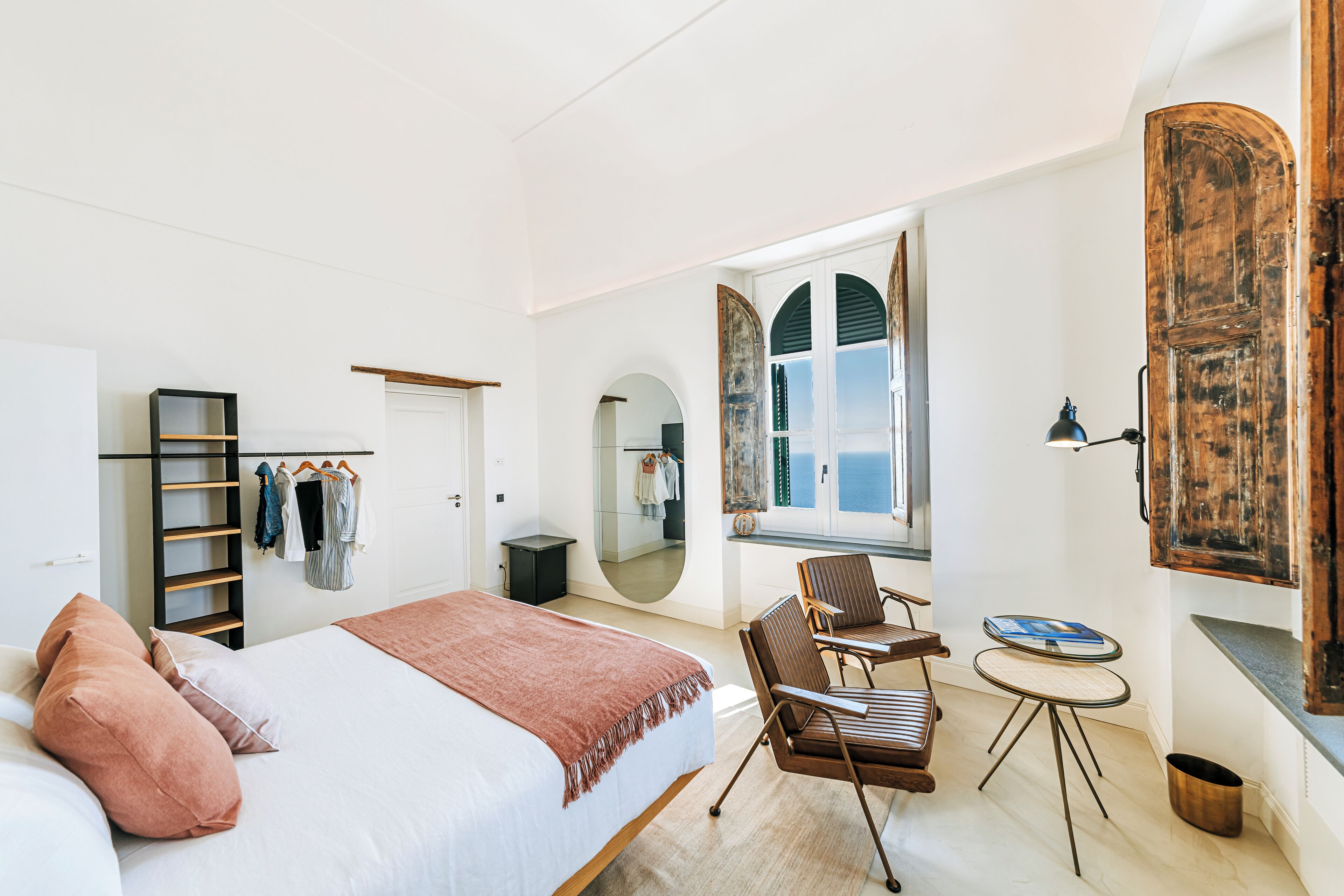 A bedroom with a bed, a chair, a small table, a mirror, and a wardrobe.
