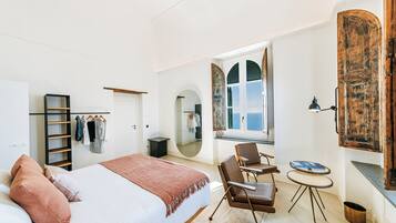 A bedroom with a bed, a chair, a small table, a mirror, and a wardrobe.