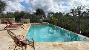 En swimmingpool med stenvægge, to fletstole og en stensokkel.