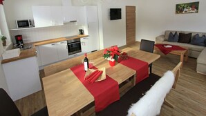 A modern kitchen with white cabinets, a microwave, and a coffee maker. There is a dining area with a wooden table, red tablecloths, and a chandelier. A sofa and a painting are visible in the living room. - Apartment in Aschau near Hochzillertal Slopes (Aschau im Zillertal)