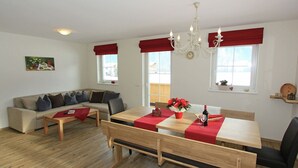 A modern living room with a sofa, a dining table with benches, a chandelier, and large windows with red curtains. - Apartment in Aschau near Hochzillertal Slopes (Aschau im Zillertal)