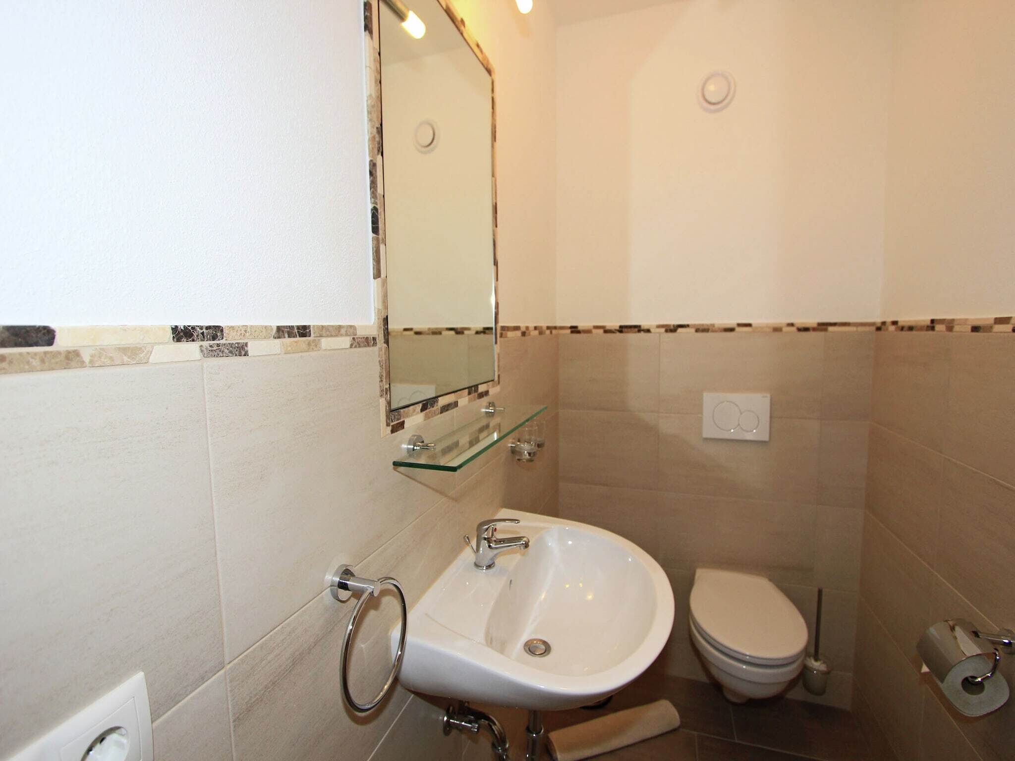 Une salle de bain avec un lavabo blanc, une étagère en verre, des toilettes et un miroir.