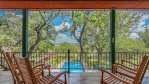 A covered patio with wooden rocking chairs, a view of a swimming pool, and a fenced garden area. - Perfect Summer Lakefront Escape- Pool/Outdoor Kitchen & BBQ/Hot Tub/Fire Pit (Canyon Lake)