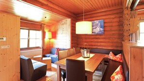 Ein gemütliches Blockhaus-Interieur mit Esstisch aus Holz, gepolsterten Sitzmöglichkeiten und einem großen Fenster.