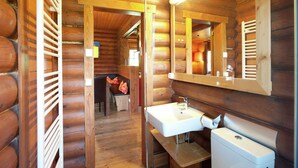 Ein Badezimmer in einer Holzblockhütte mit einer hölzernen Bank, einem Waschbecken, einer Toilette und einem Spiegel.