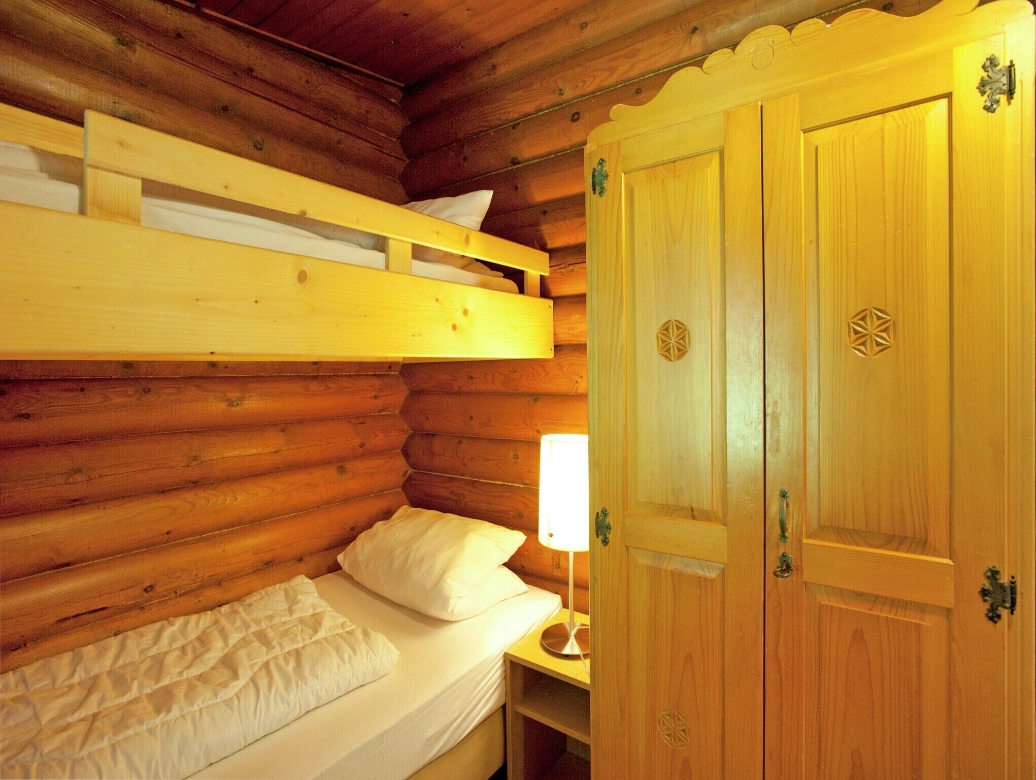 A wooden cabin room with a bunk bed, a single bed, and a wooden wardrobe with decorative metal handles.