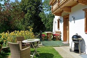 Une terrasse dotée de meubles en osier, d’un barbecue et d’un jardin agrémenté de fleurs jaunes.