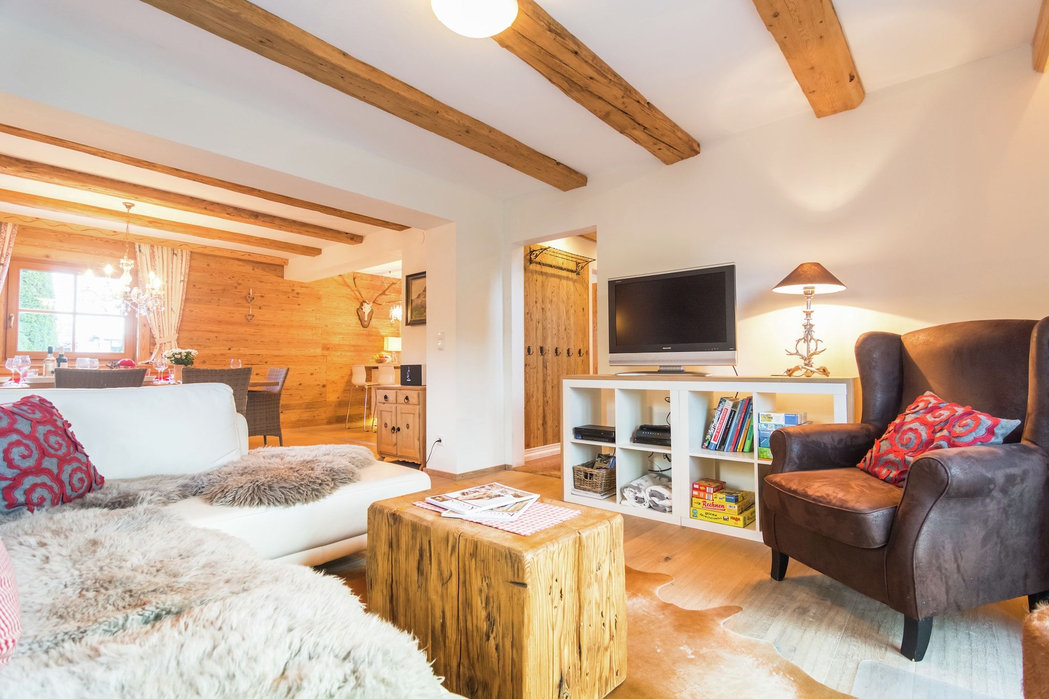 Ein gemütliches Wohnzimmer mit Holzbalken, einem weißen Sofa, einem braunen Ledersessel und einem Holztisch.