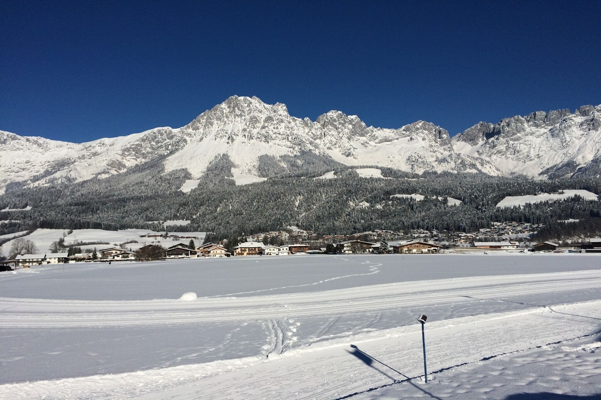 Schneebedeckte Landschaft mit einem Gebirgszug im Hintergrund und einem ebenen, schneebedeckten Feld im Vordergrund.