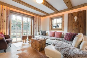 A cozy living room with a large window, wooden beams, a white sofa, and a deer skull on the wall. - Chalet in Ellmau near Ski Slopes (Ellmau)
