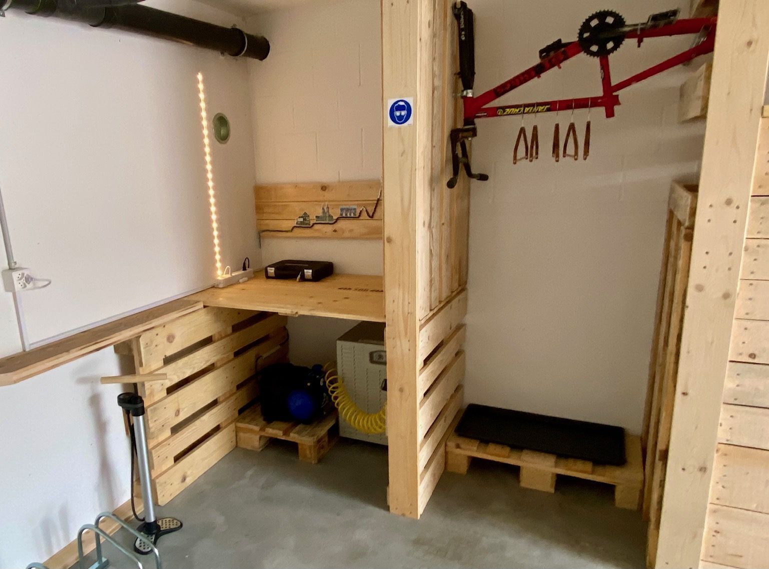 Una habitación pequeña con un escritorio de madera, una bicicleta roja y un estante con objetos.