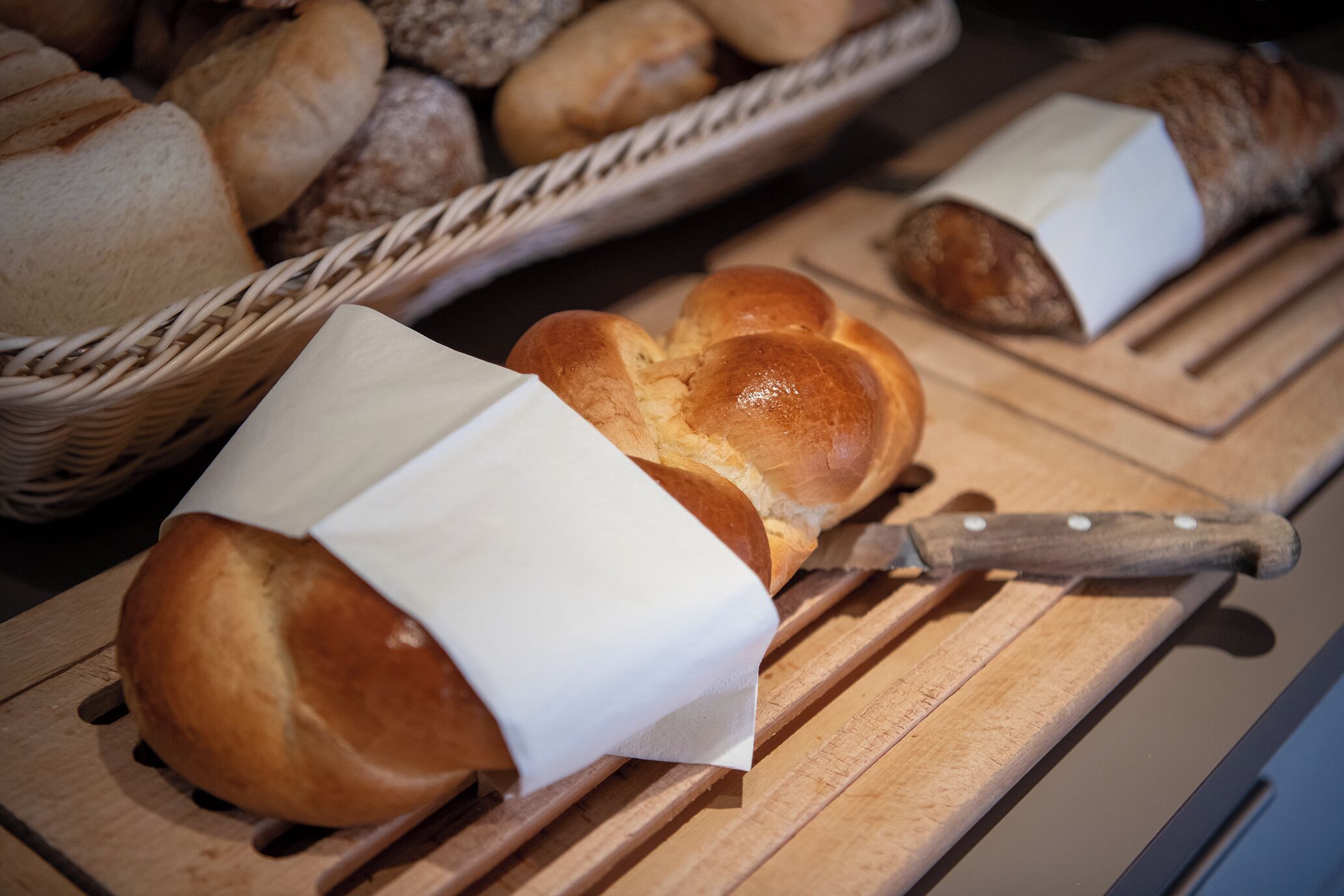 Uma tábua de corte de madeira com uma faca e vários pães, alguns enrolados em papel.