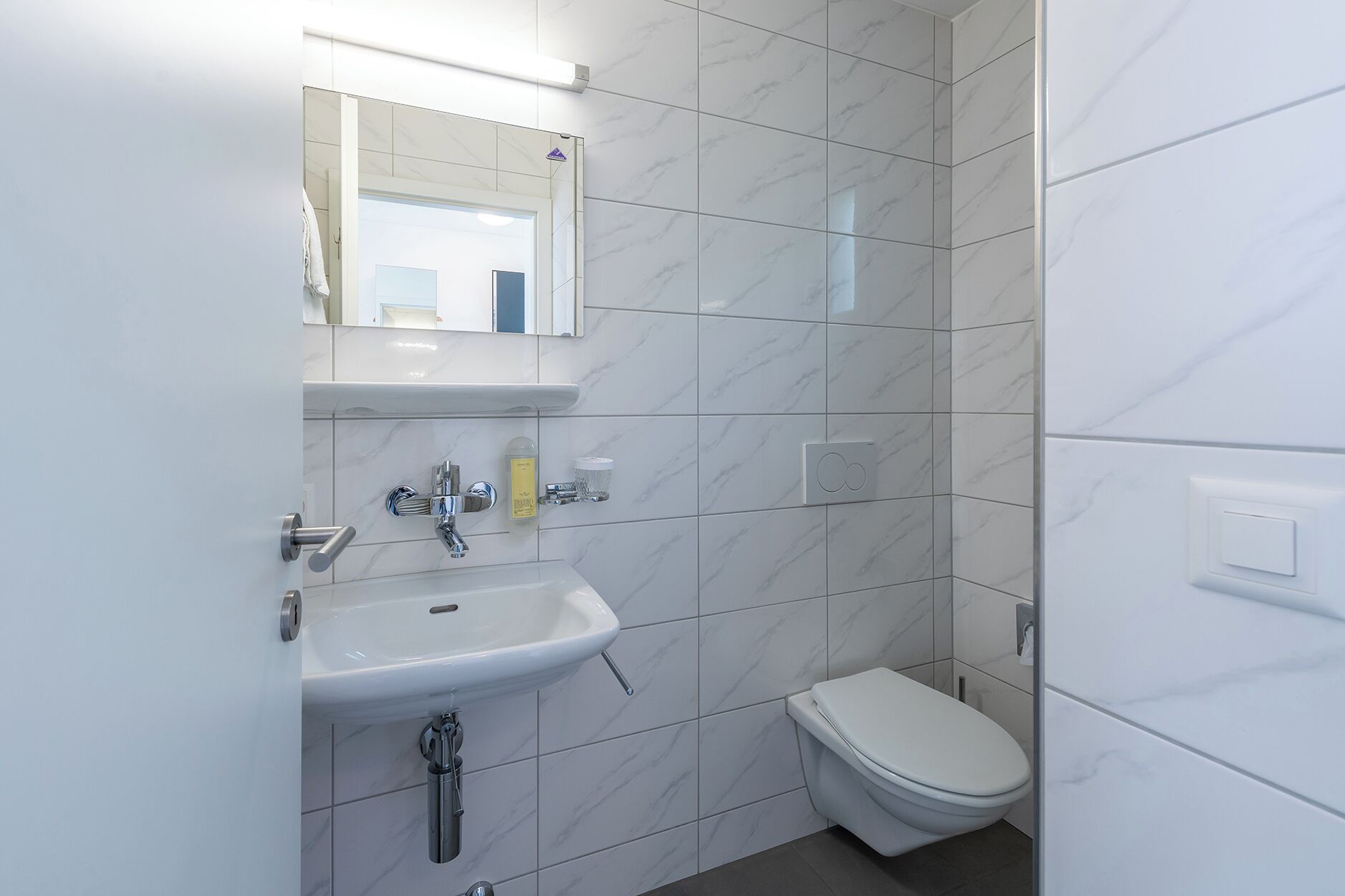 Un baño moderno con un lavamanos blanco, un espejo y un inodoro.