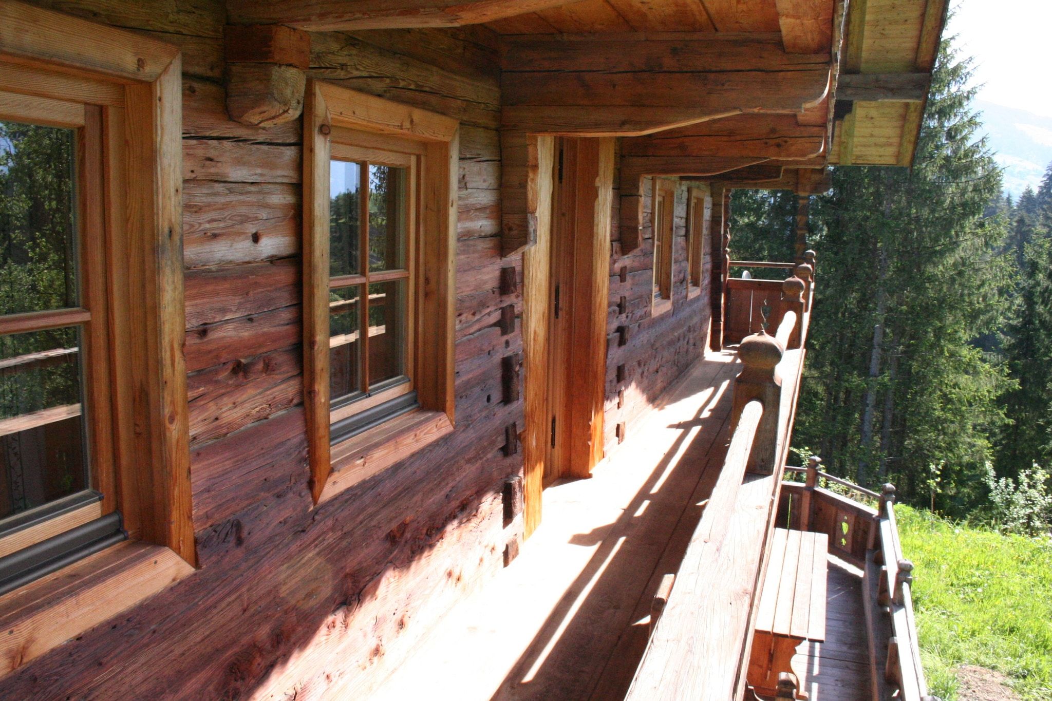Una cabana de fusta amb diverses finestres i un balcó amb vista a una zona boscosa.