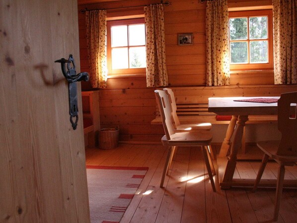 A wooden cabin interior with a dining table, chairs, and a window with curtains. - Farmhouse in Hopfgarten near SkiWelt (Hopfgarten im Brixental)