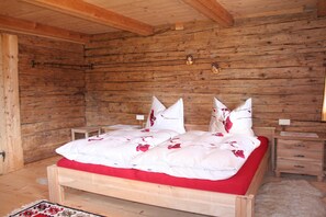 A wooden cabin bedroom with a bed, two bedside tables, and a nightstand. - Farmhouse in Hopfgarten near SkiWelt (Hopfgarten im Brixental)