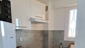 Une cuisine compacte avec des meubles blancs, un four encastré, un grille-pain et un lave-vaisselle.