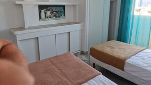 Une chambre d’hôtel comprenant un lit, une table de chevet, un miroir, une étagère avec des objets décoratifs et une fenêtre avec des rideaux.