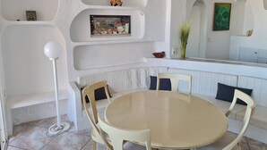 Un espace repas moderne avec une table ronde et des chaises, des murs blancs et des étagères intégrées ornées d’objets décoratifs.
