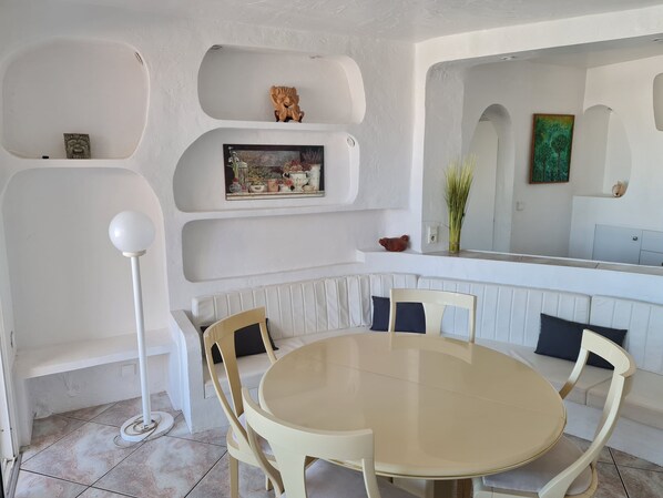 A modern dining area with a round table and chairs, white walls, and built-in shelves with decorative items. - Quiet seafront location in a premium gated community, ideal family accommodation (Théoule-sur-Mer)