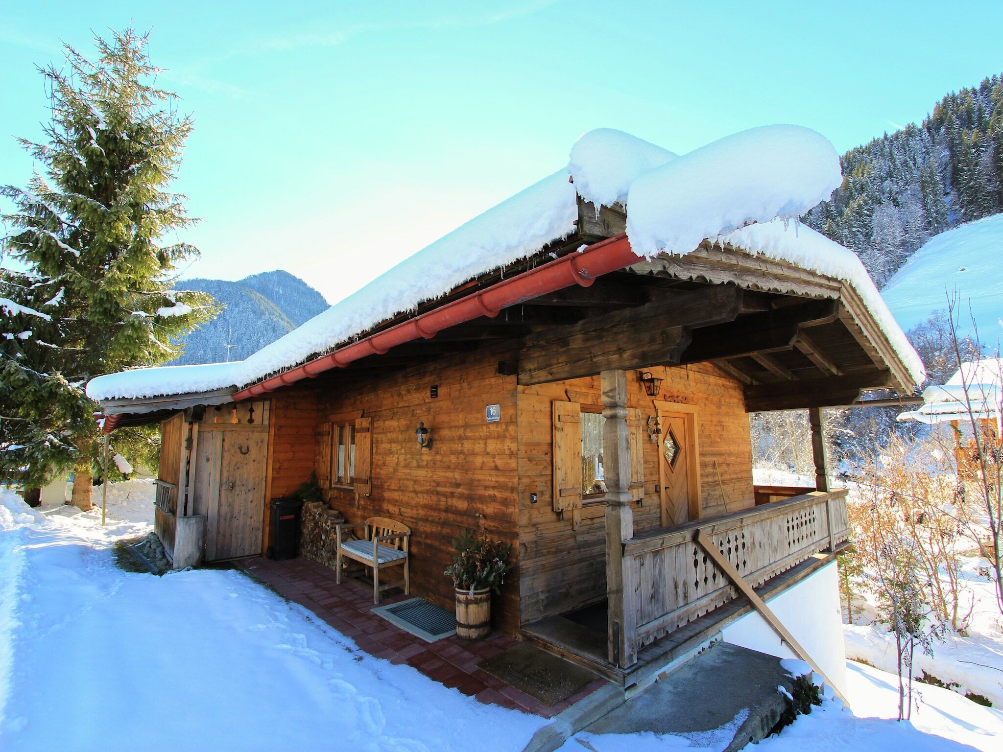 Una cabaña de madera con techo nevado y un porche con banca.