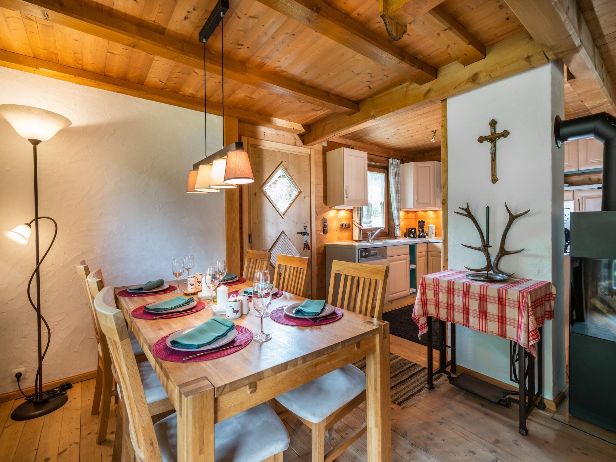Ein Holzespeisetisch ist mit Tellern, Gläsern und Besteck gedeckt, im Hintergrund ist eine Küche zu sehen.