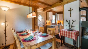 Una mesa de comedor de madera dispuesta con platos, vasos y cubiertos, con una cocina al fondo.