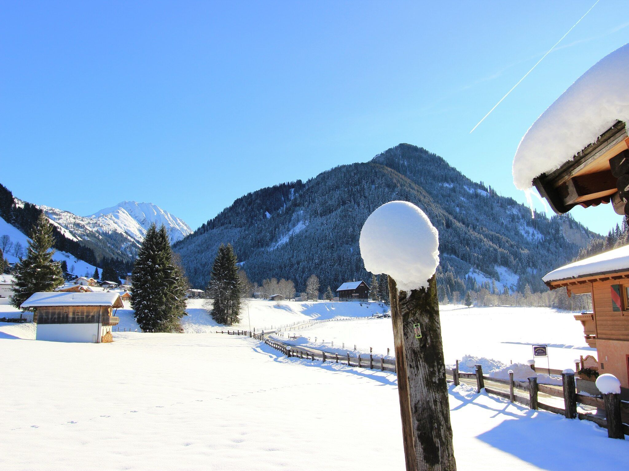 Un paysage enneigé avec une clôture en bois, une boule de neige posée sur un poteau et une montagne en arrière-plan.