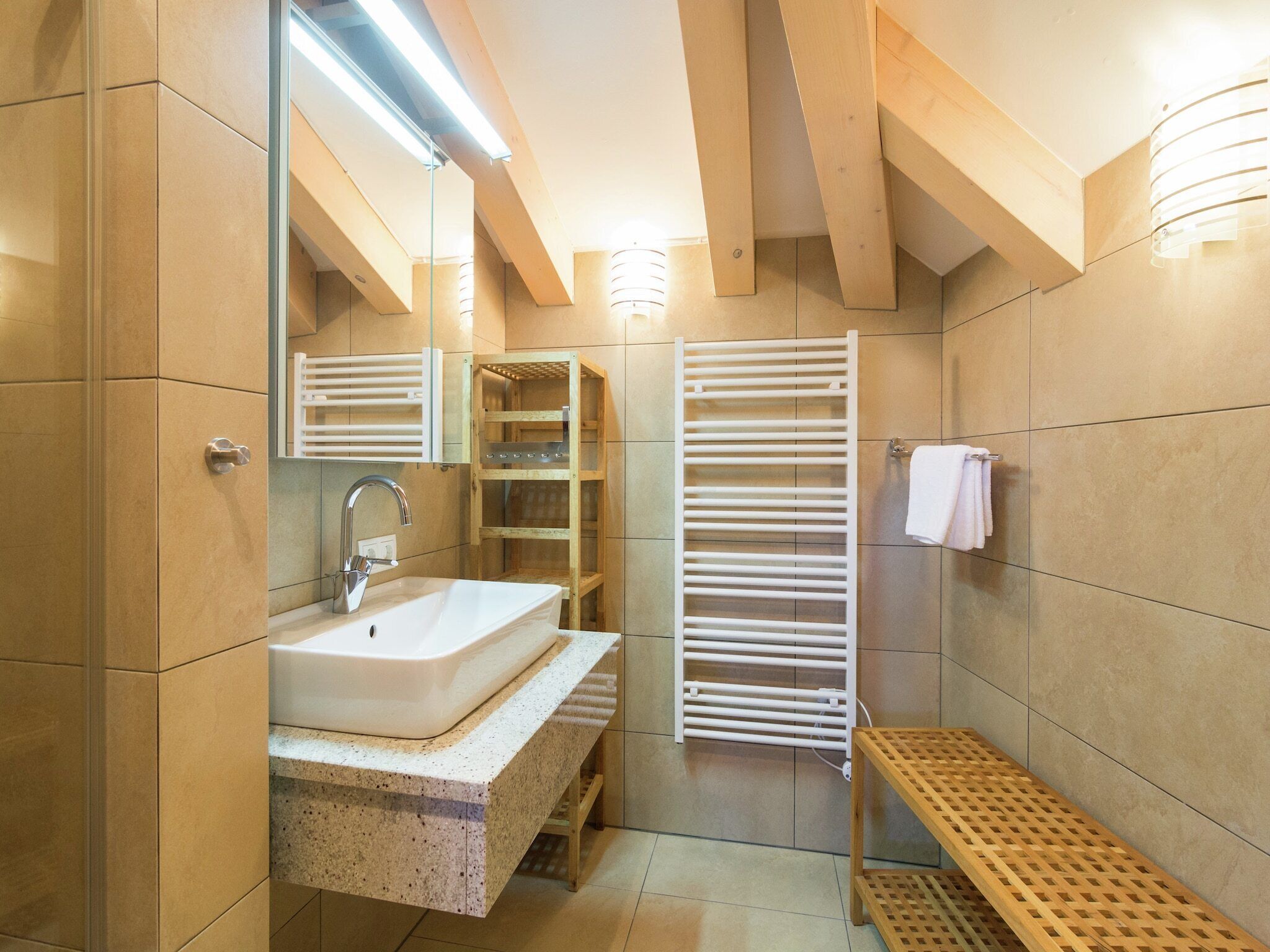 Un baño moderno con un lavabo blanco, un espejo, un toallero y un estante de madera.